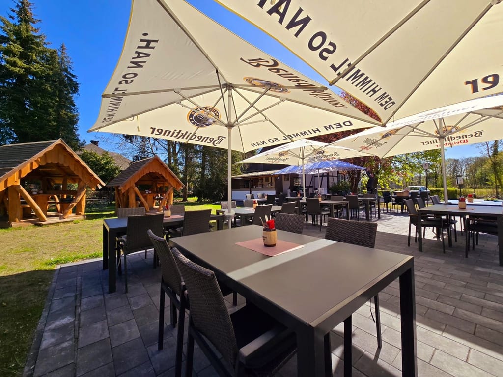 Biergarten der Westfalenschänke mit Sonnenschirmen und Holzhütten