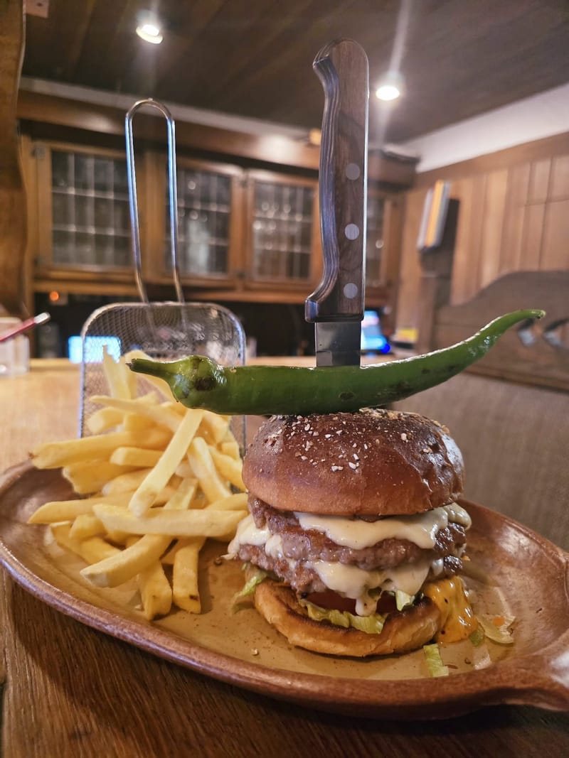 Hammer Burger mit Peperoni, Messer und Pommes Frites auf einem Holzbrett