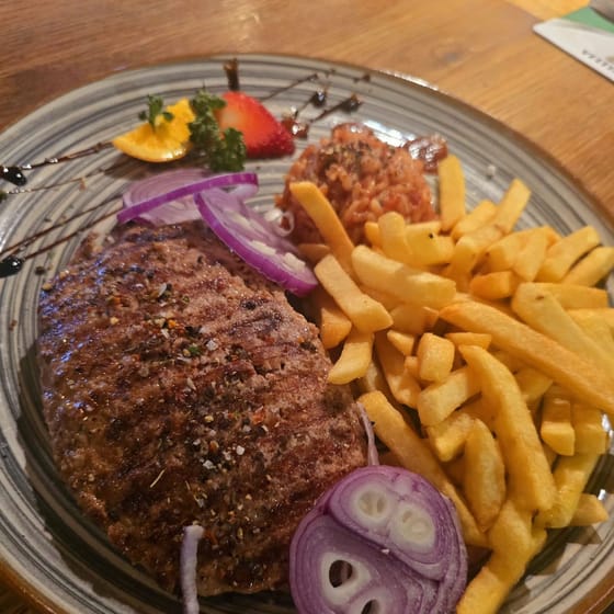 Pljeskavica mit Pommes Frites, roten Zwiebeln und Djuvec-Reis auf einem grau-blauen Teller